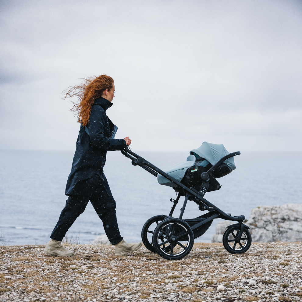 mulher caminhando com o carrinho Thule Urban Glide 3 em frente a parede de madeira.