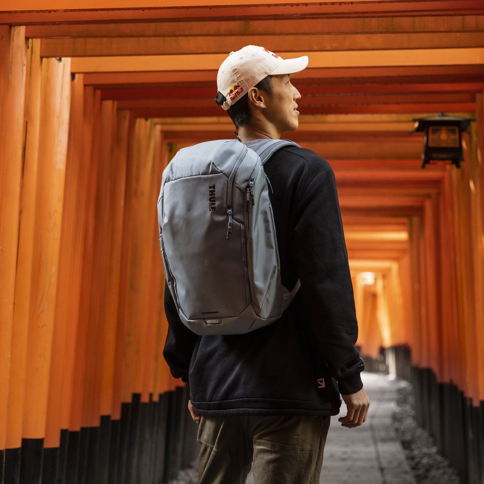 A man with a white baseball cap is standing in an orange alley way with a blue Thule Chasm backpack.