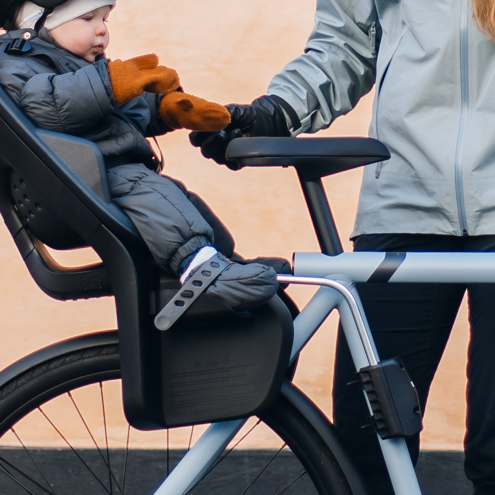 A baby sits on a rear child bike seat with the help of the Thule Quick Release Bracket.