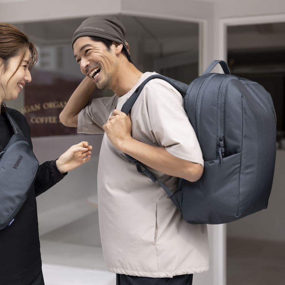 A woman and man laugh, one carrying a blue Thule Subterra backpack, the other a blue Thule Subterra sling.
