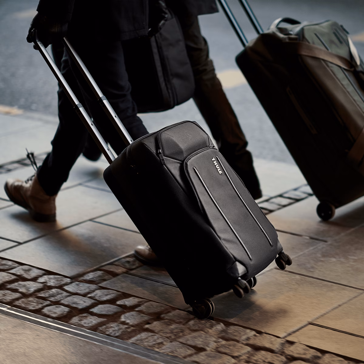 Two people walkd down a rainy sidewalk with Thule Crossover 2 Expandable Carry-on suitcases.