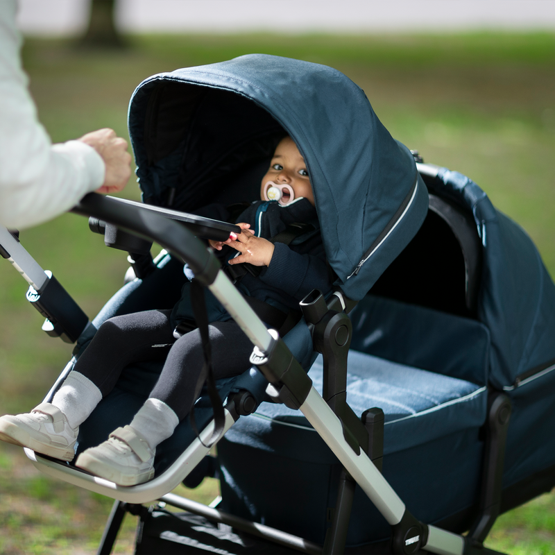 A baby sits in a blue double stroller thanks to  the Thule Sleek Adapter Kit.