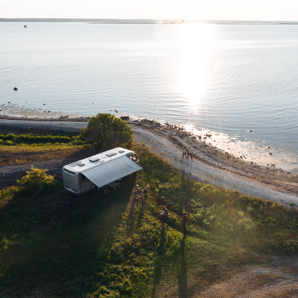 A motorhome is parked next to a lake where the sun is setting and it has a Thule Omnistor 8000 RV awning.