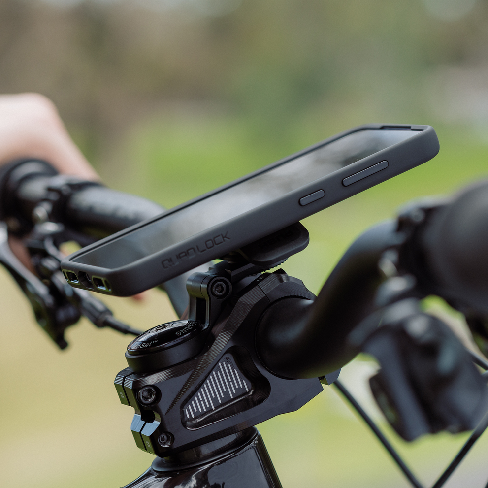 Smartphone attached to a Quad Lock adjustable stem cap mount on a bicycle handlebar during outdoor use.
