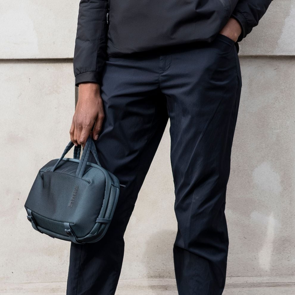 A close-up of someone wearing all black, holding a blue Thule Subterra Crossbody 5L.