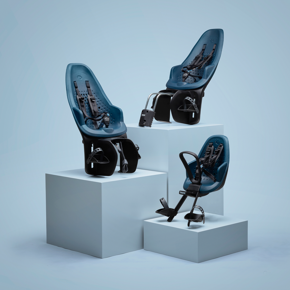 Tres asientos de bicicleta para niños Thule Yepp 2 color tostado están sobre un pedestal con un fondo tostado.