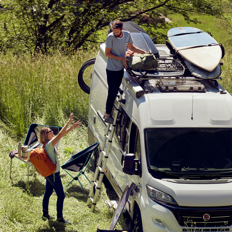 A person unloads items from their van by climbing up the Thule Van Ladder 9 van steps.