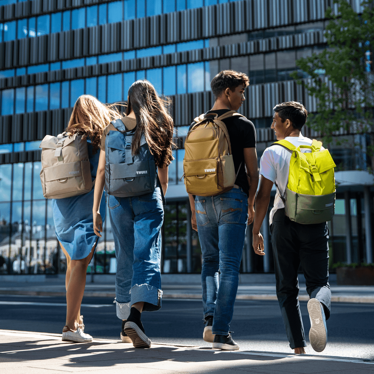 Four friends walk down a city street carrying Thule Departer backpacks in various colors.