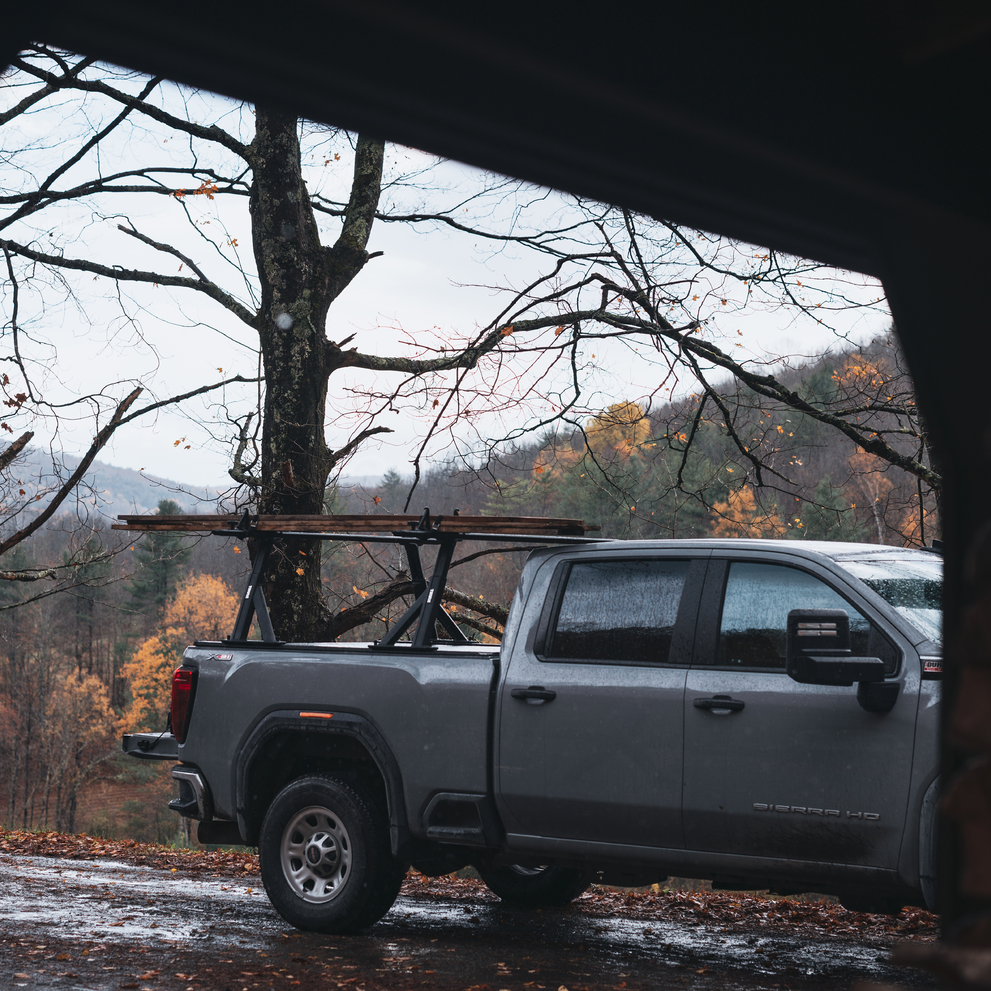 A vehicle with the Thule Xscape truck rack that carries wooden boards in an outdoors environment.