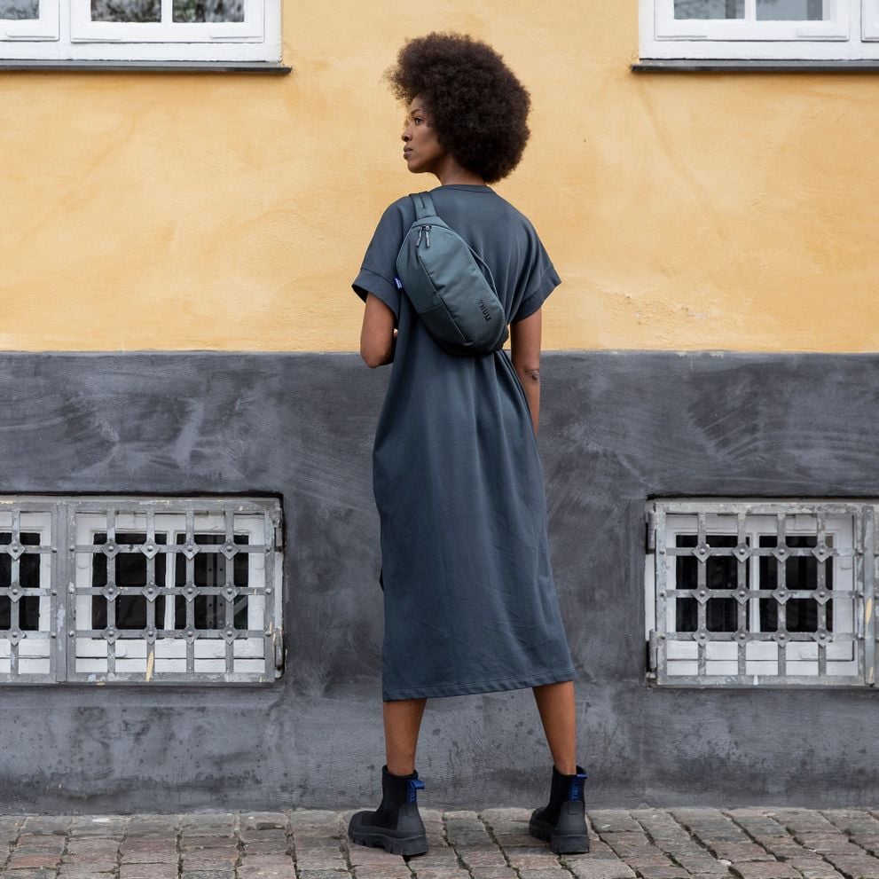 A woman stands with her back to the camera, with a Thule Subterra sling bag on her back.