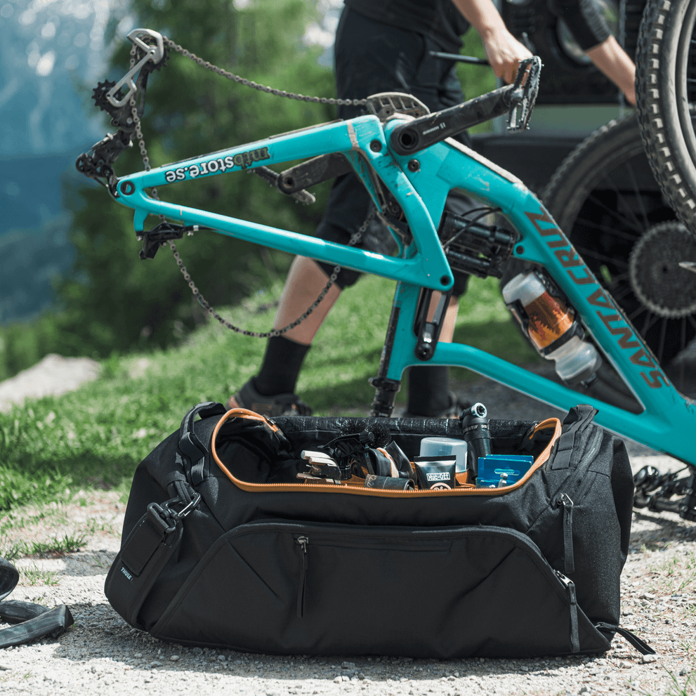 In the countryside, a person fixes their blue bike using gear from a Thule Roundtrip bike gear duffel.