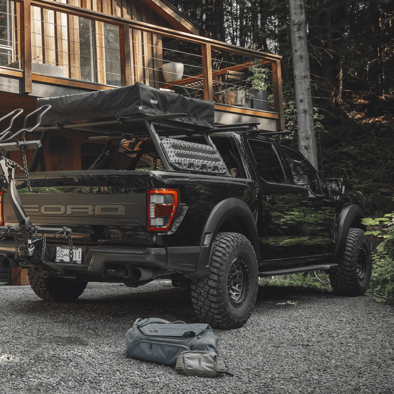 A pickup truck with a Thule Xscape truck rack loaded with gear outside a cabin, ready for adventure.