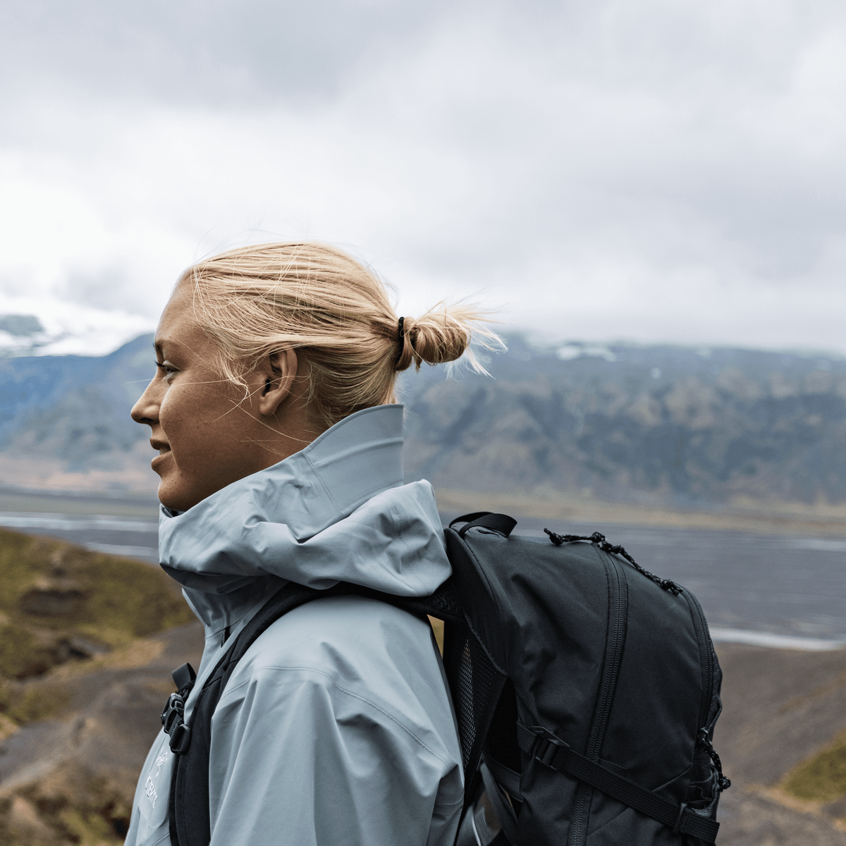 A hiker walks on a cloudy day on a mountain path carrying aThule Nanum 25L  hiking backpack.