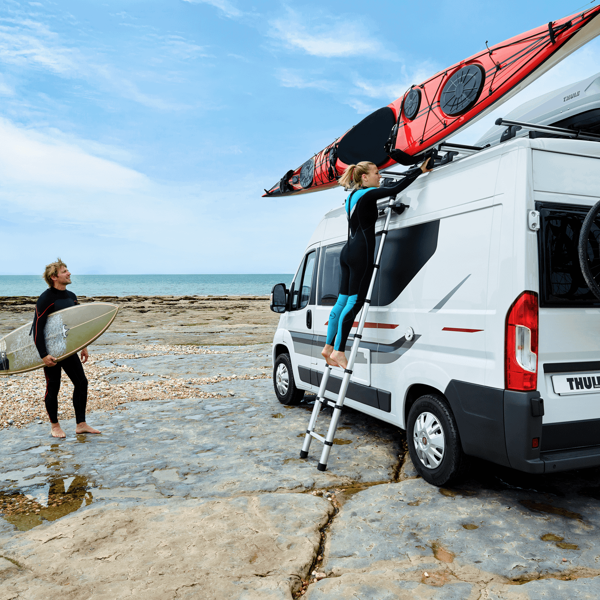 A woman is mounting a kayak on the roof of a van with a Thule Hullavator Pro