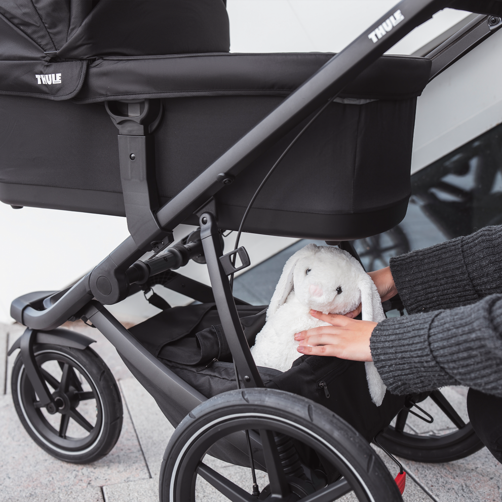 A close-up of a parent putting a toy inside the cargo basket under a Thule Urban Glide 2 bassinet.