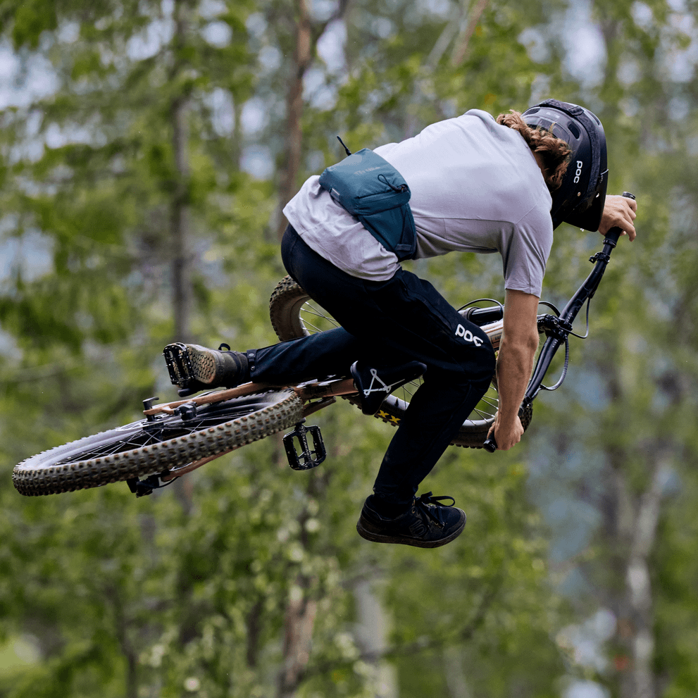 A mountain biker on their bike in the air are carrying a Thule Rail 0L hydration Hip Pack.