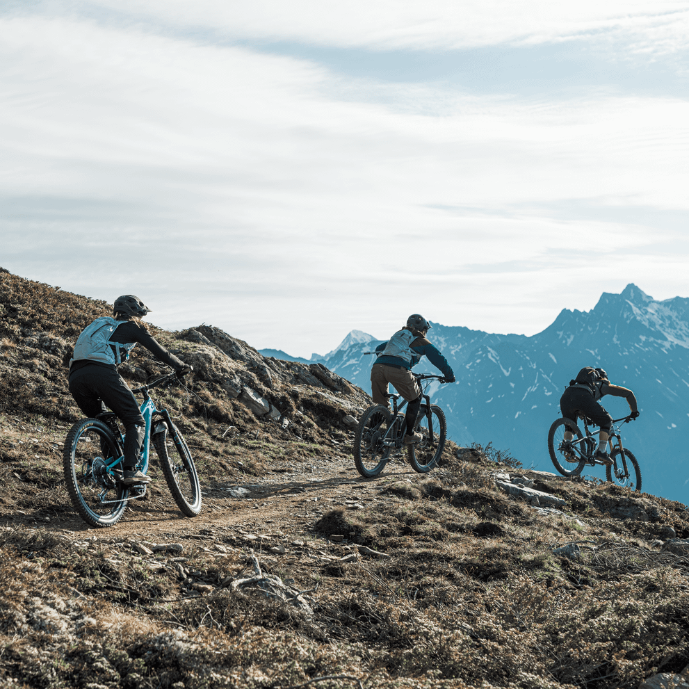 Three cyclists ride on a mountain path carrying blue Thule Vital 3L Women's Hydration Backpacks.