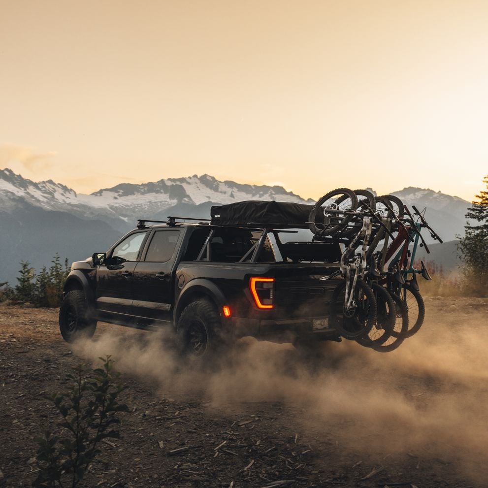 Thuole pickup truck with the vertical Thule ReVert hitch bike rack fully loaded with mountain bikews, is driving in the mountains.