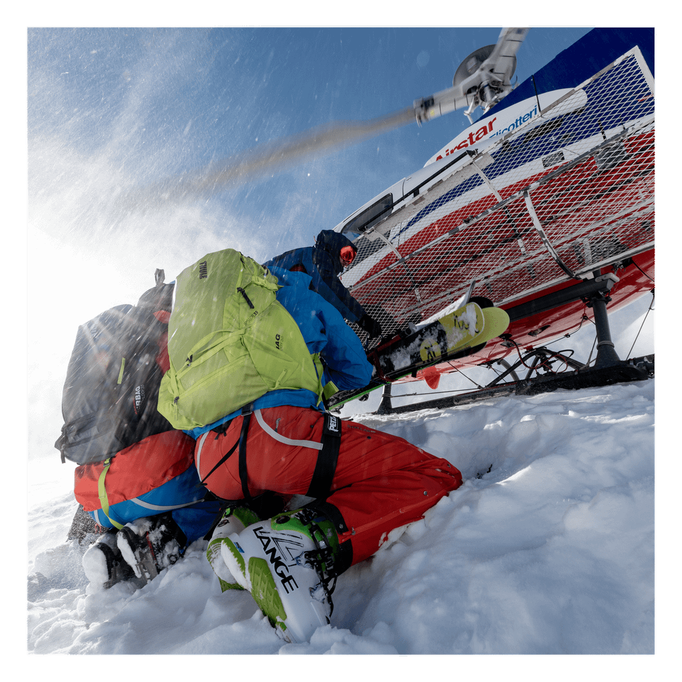 Two people kneel in the snow carrying Thule UpSlope ski backpacks.
