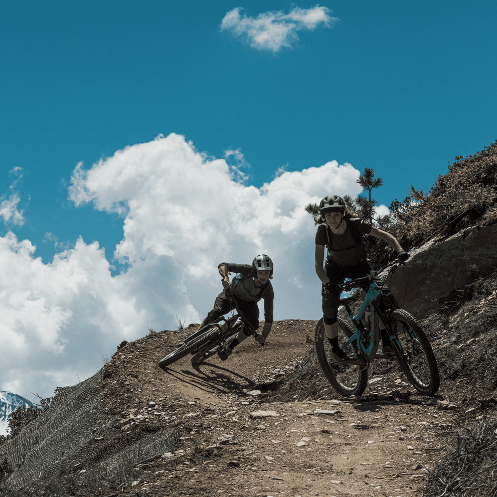 Two cyclists go mountain biking down a mtb trail high up in the mountain  with a Thule Vital hydration pack.