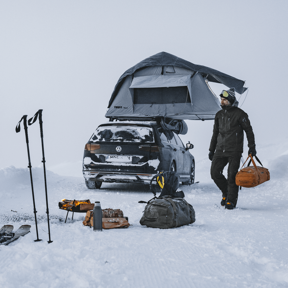 Two people are standing in the snow with their ski gear, close to a car with a Thule Tepui Kukenam roof top tent