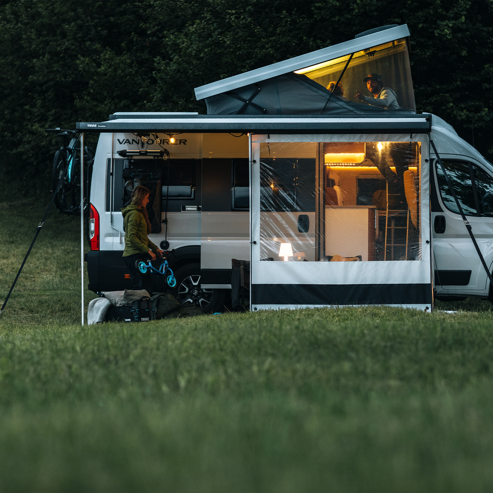 A van parked in the grass at night with an awning and a Thule 3rd Support Leg.