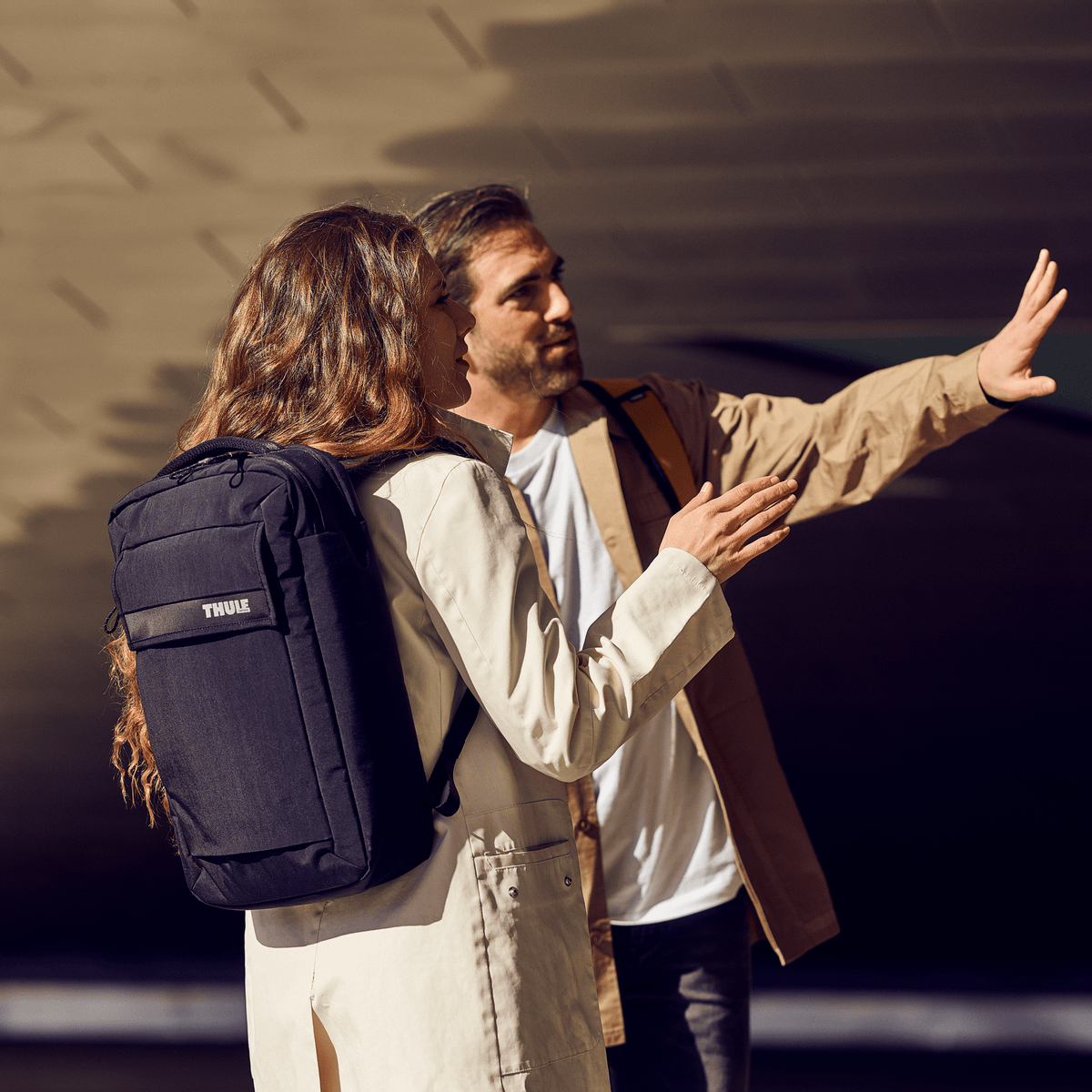 Two people point into the distance, one carrying a Thule Paramount Convertible Laptop Bag.