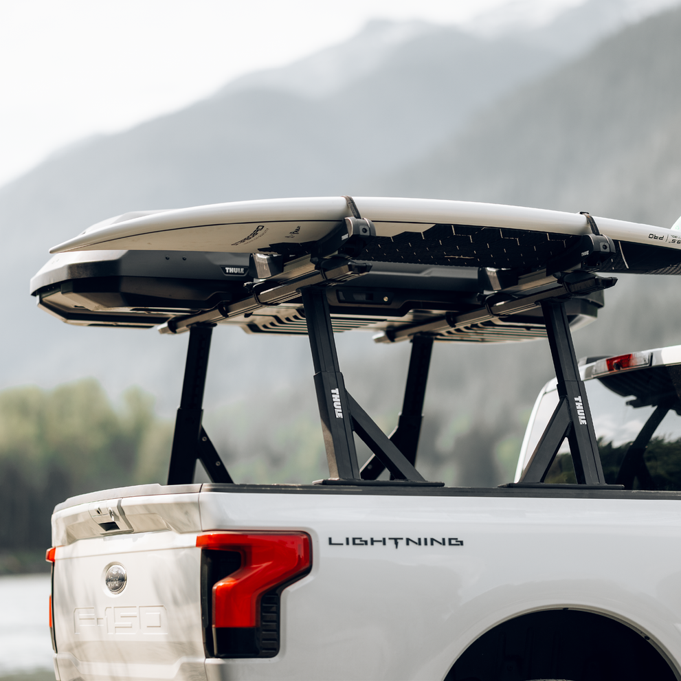Close-up of Thule Xscape truck rack installed on truck bed, with a roof box and a SUP board.