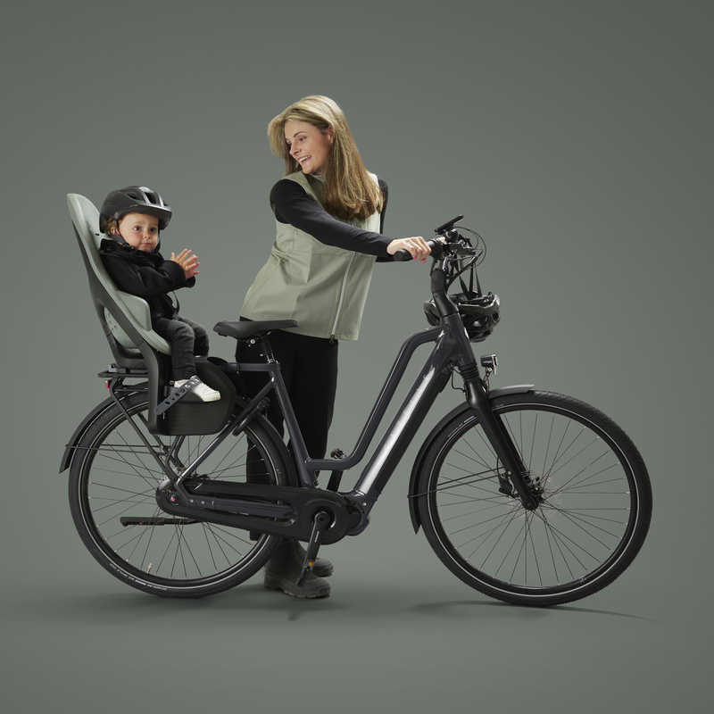 Une femme est debout à côté de son vélo, regardant en arrière son enfant assis dans un siège de vélo pour enfant.