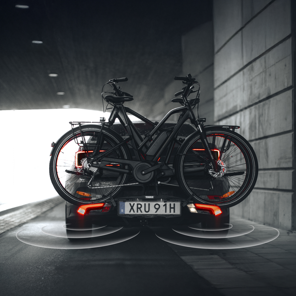 Thule Epos ParkSecure bike rack with active parking sensors, mounted on the back of a car carrying two bikes and parked in an urban setting.