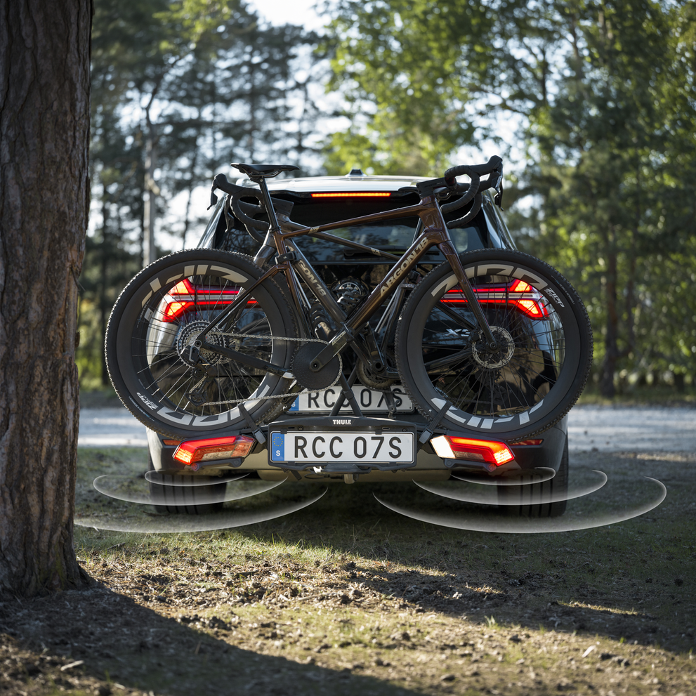 Rear view of a car with a Thule Epos ParkSecure bike carrier mounted on the towbar, carrying a road bike with the parking sensors on.