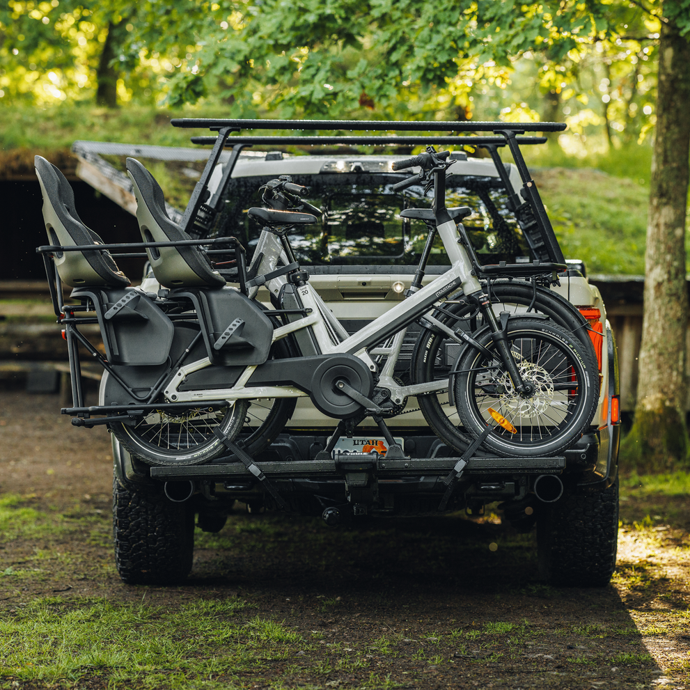 Two heavy e-bikes are secured on the Thule Vero hitch bike rack mounted on the back of a truck parked in an outdoor setting.