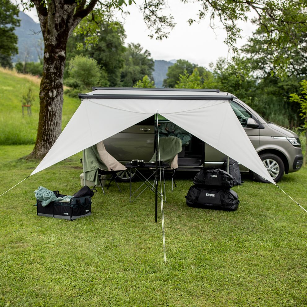 A van is parked in the grass with Thule Subsola versatile awning panels.
