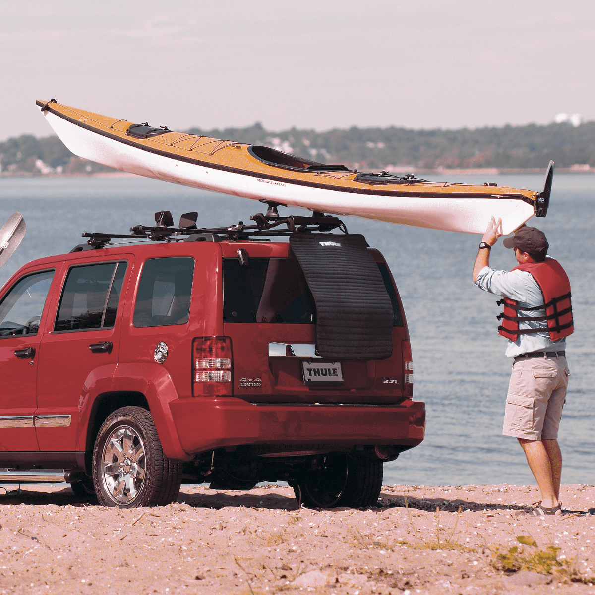 A man is loading a kayak on a Thule WaterSlide kayak carrier on his car