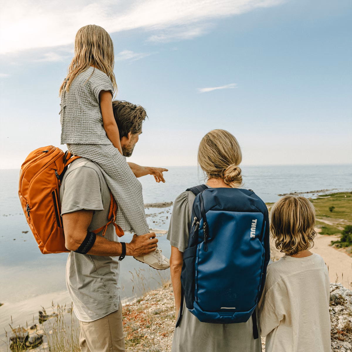 A family stands on a mountain looking at the ocean, holding Thule Chasm backpacks.