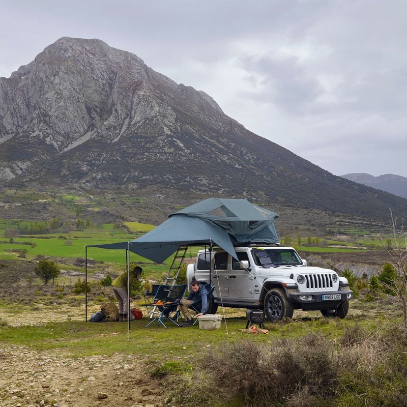 A car with a roof top tent and an awning is parked in front of a mountain