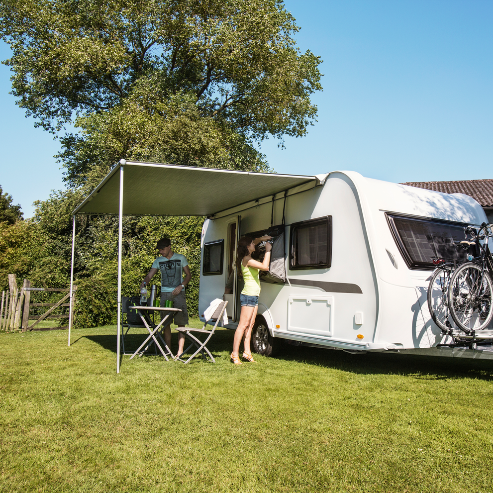 A woman gets something out of a bag outside a caravan with a Thule Omnistor 1200 caravan awning.