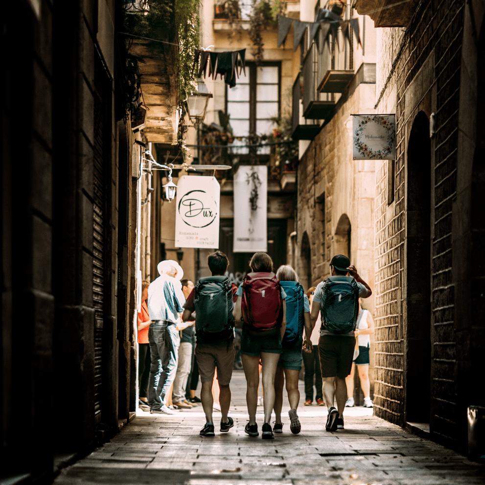 A group of friends walk down a narrow city street carrying blue and red Thule Landmark 40L backpacking backpacks.