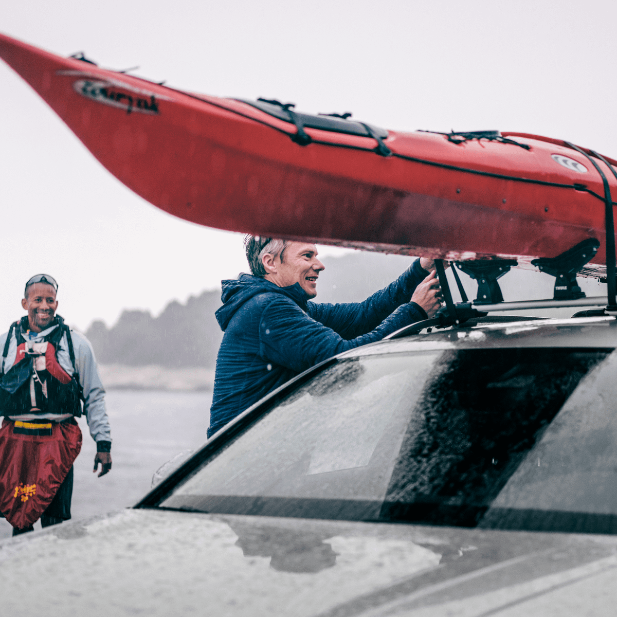 Closeup of a man fastening a kayak on a car roof with a Thule Dockgrip with another man in the background