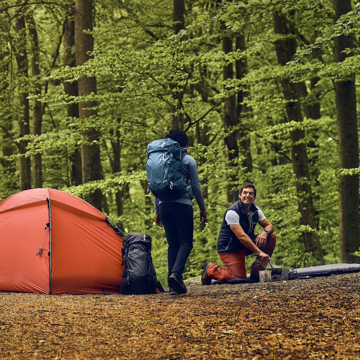 Two people go camping in the woods, carrying Thule Versant hiking backpacks.