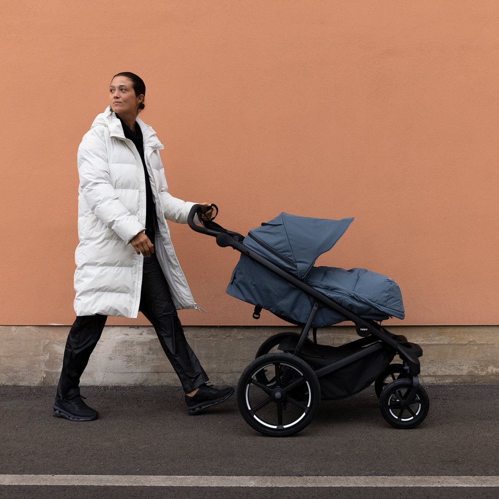 Parent pushing a stroller outdoors, with the baby inside protected by the Thule Elements high-performance footmuff.