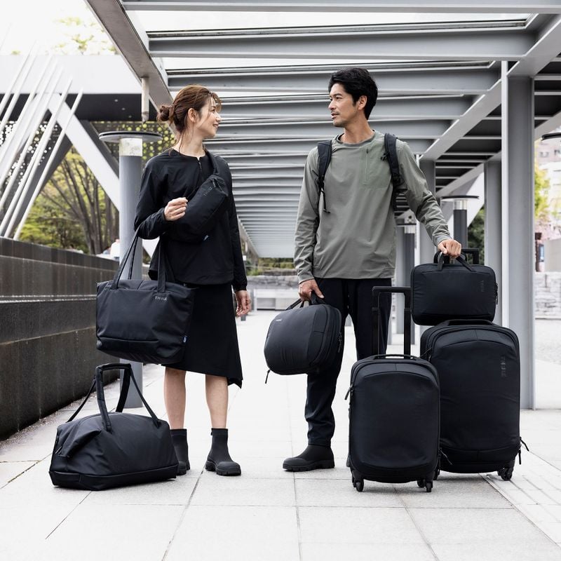 A man and woman walk down a street holding all the Thule Subterra luggage.