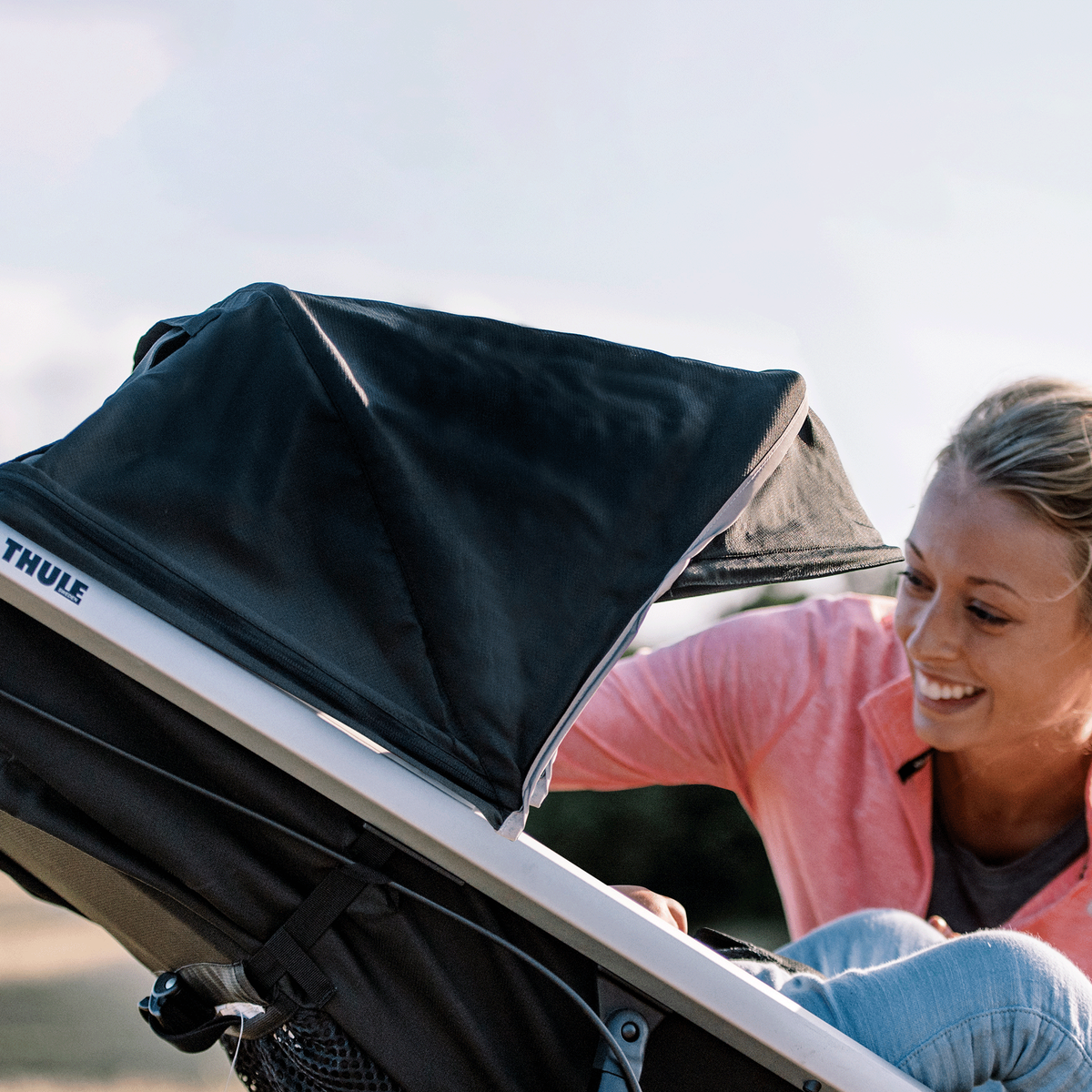 A close-up of a woman kneeling down to tend to her child in a black Thule Glide 2 jogging stroller.