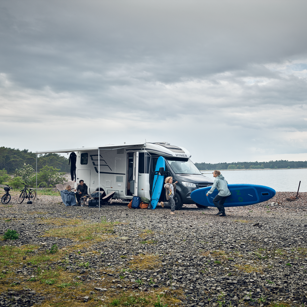 A motorhome with a Thule Omnistor 5200 rv awning is parked next to a lake on a cloudy day.