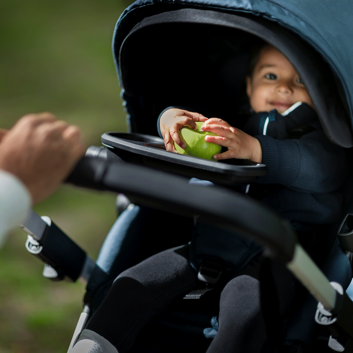 A close-up of a toddler holding an apple inside the Thule Sleek baby stroller.