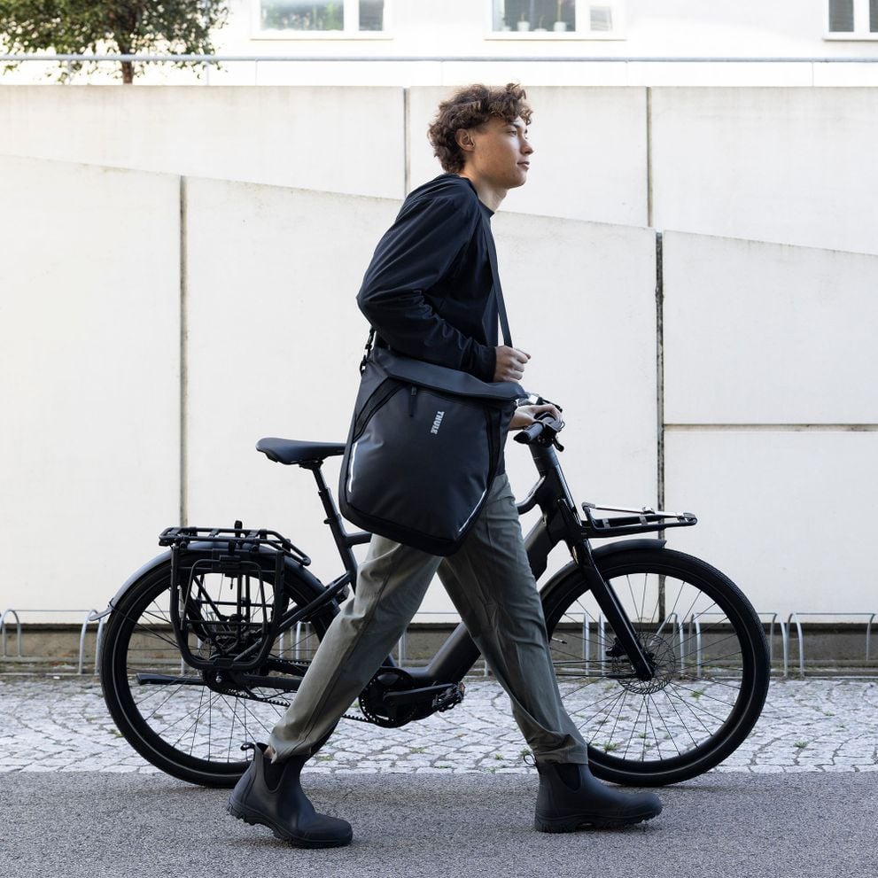 Commuter carrying a Thule Chasm bag next to a bike.