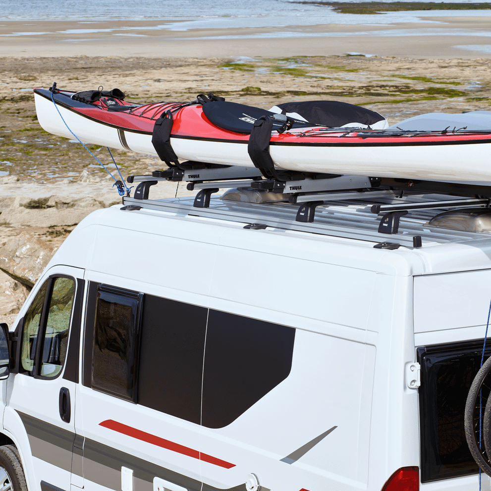 A van has a Thule ProBar Flex van rack system and a kayak installed on top.
