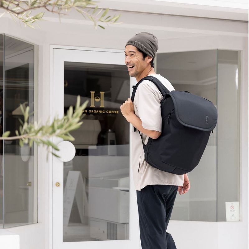 A man stands outside a white shop window with a black Thule Subterra travel backpack.