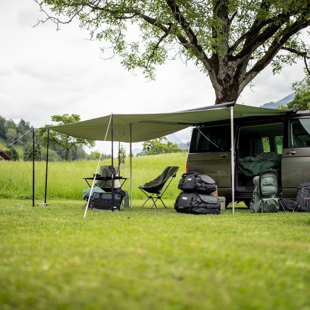 A van is parked in the grass with a camp set up under the Thule Subsola awning panels.