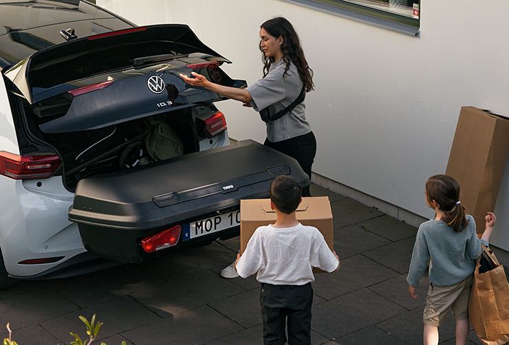 A woman and her two children loading a car with bags and packages in the trunk and in a Thule Arcos cargo box